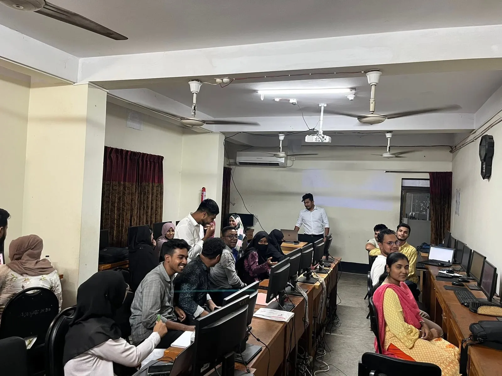 Shakawat Hridoy teaching a class of students at computer workstations in a training lab in Feni, Bangladesh