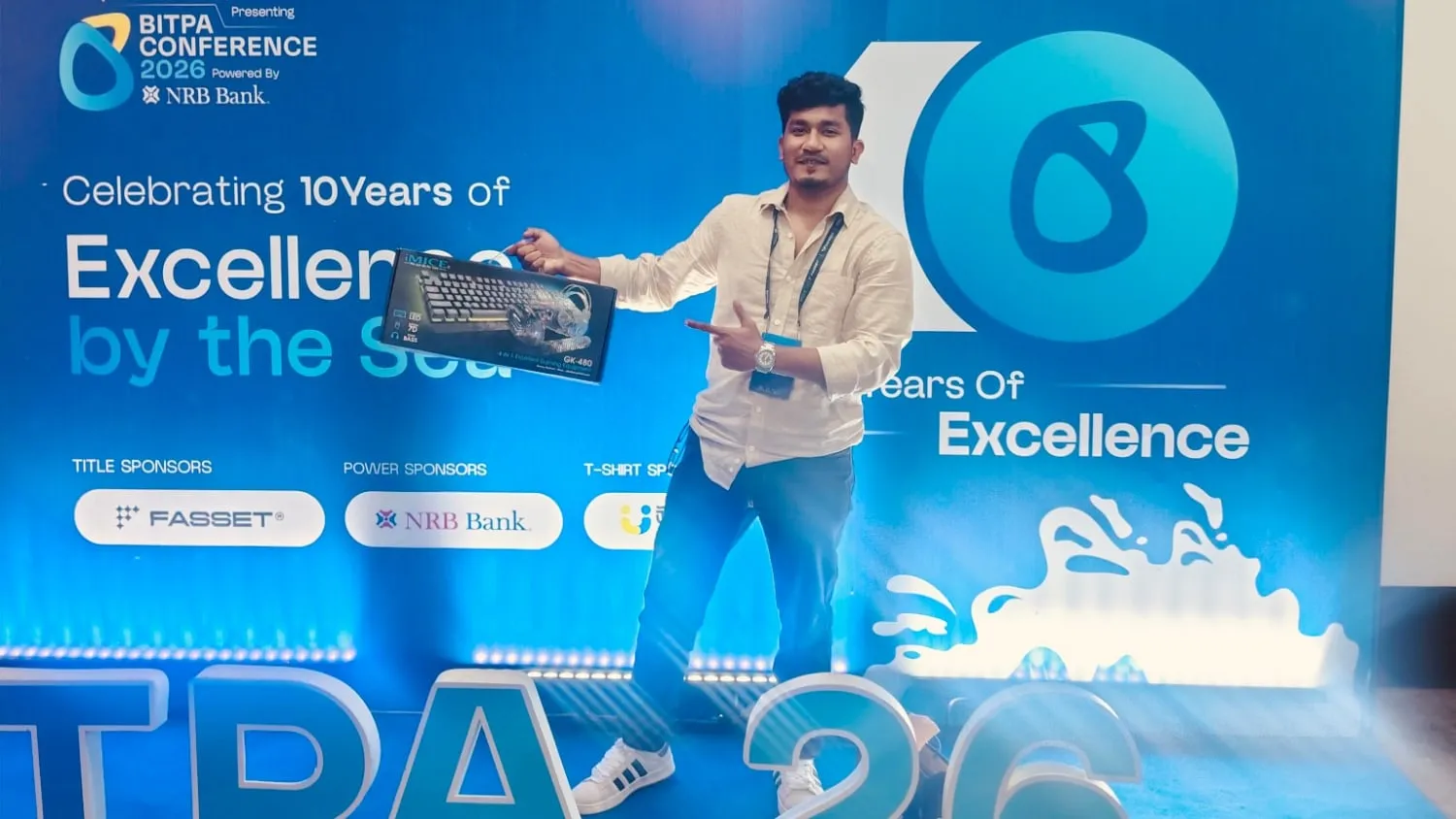 Shakawat Hridoy holding his raffle prize at BITPA Conference 2026 in Cox's Bazar, in front of the backdrop celebrating 10 years of BITPA