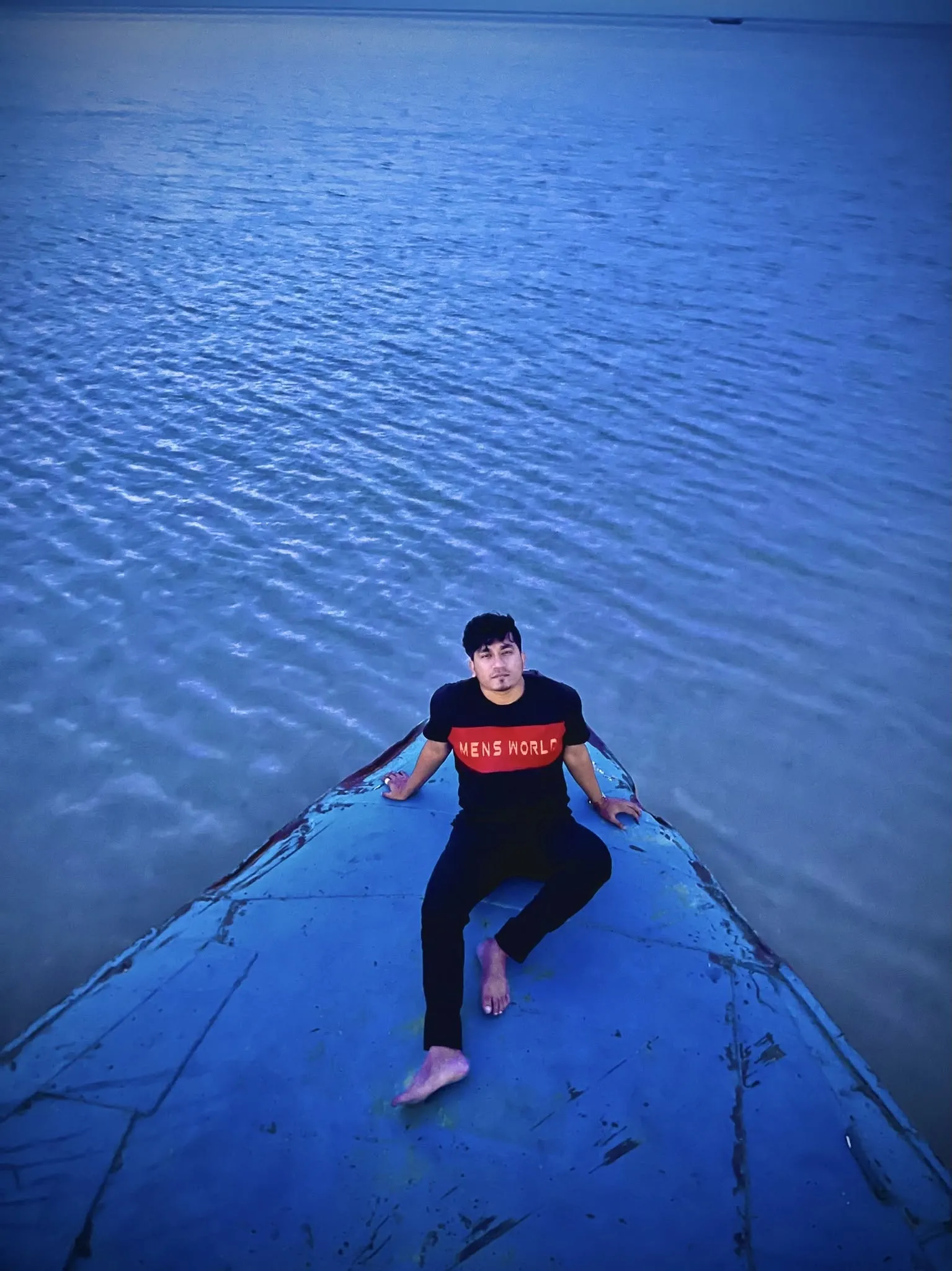 Shakawat Hridoy sitting at the bow of a wooden boat on the open water of Tanguar Haor, Sunamganj, Bangladesh