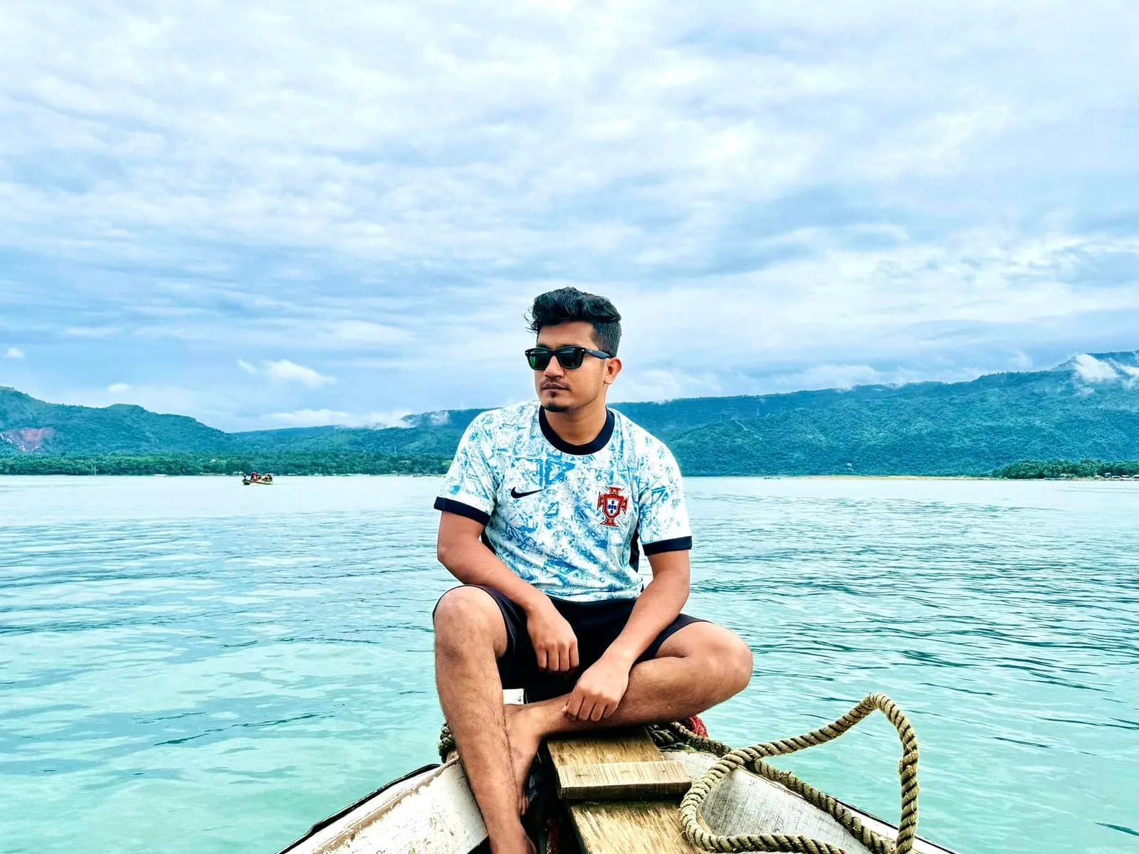 A wooden boat on the turquoise water of a lake near Tanguar Haor, with hills rising behind