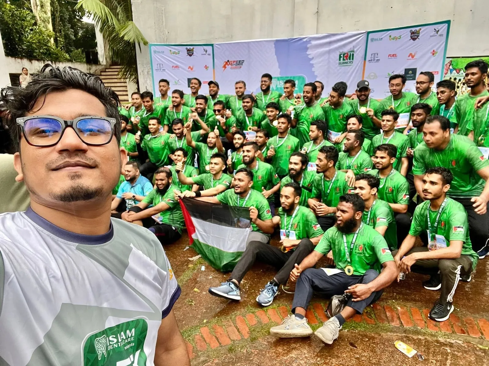 Shakawat Hridoy taking a selfie in front of a large group of runners in green shirts at a Feni Runners Community event