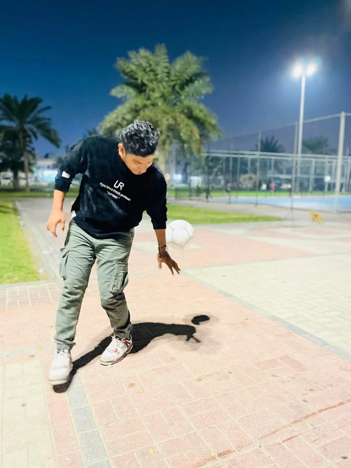 Shakawat Hridoy kicking a football on a park path in Saudi Arabia