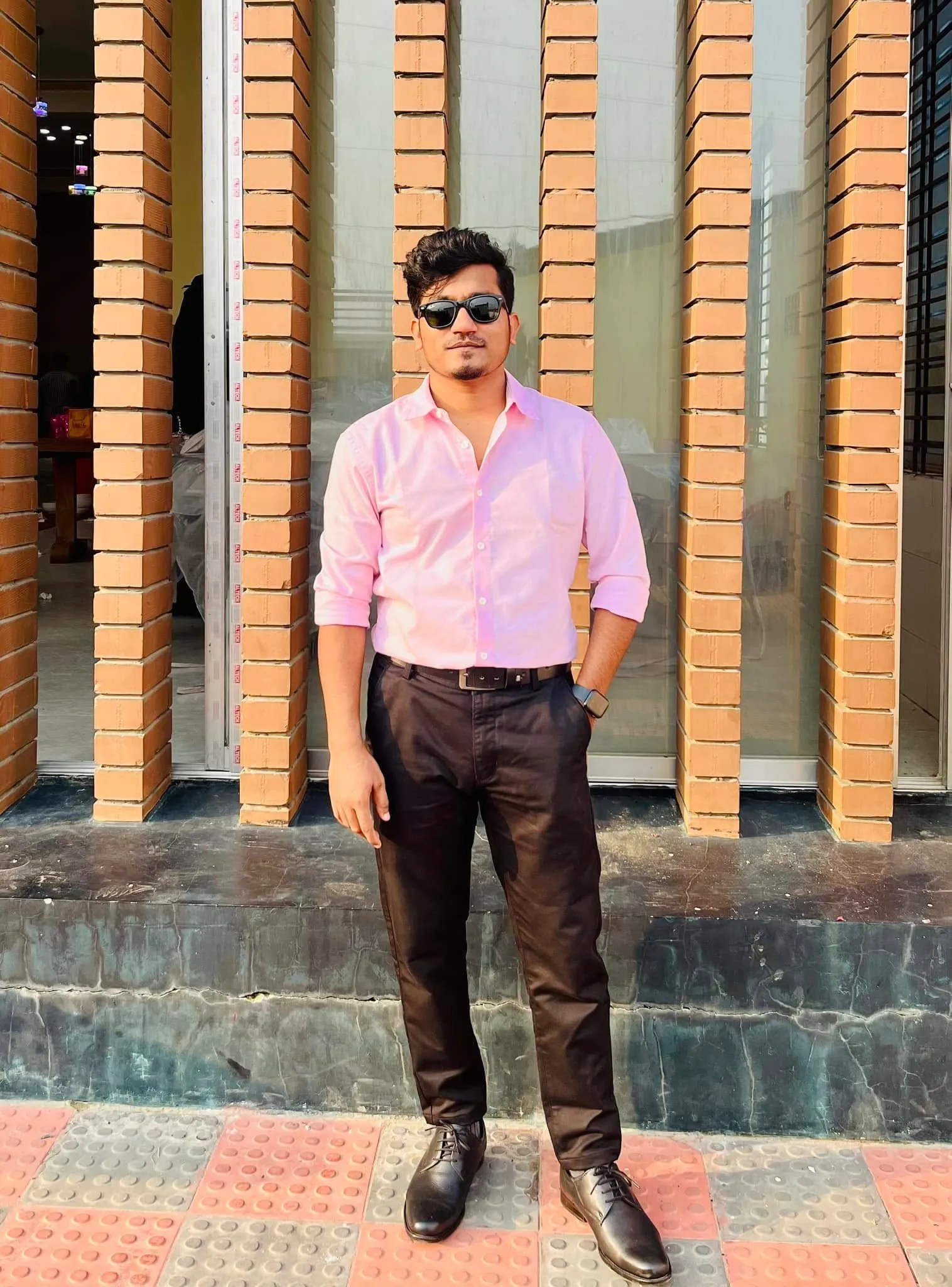Shakawat Hridoy standing outdoors in a pink shirt against a brick wall
