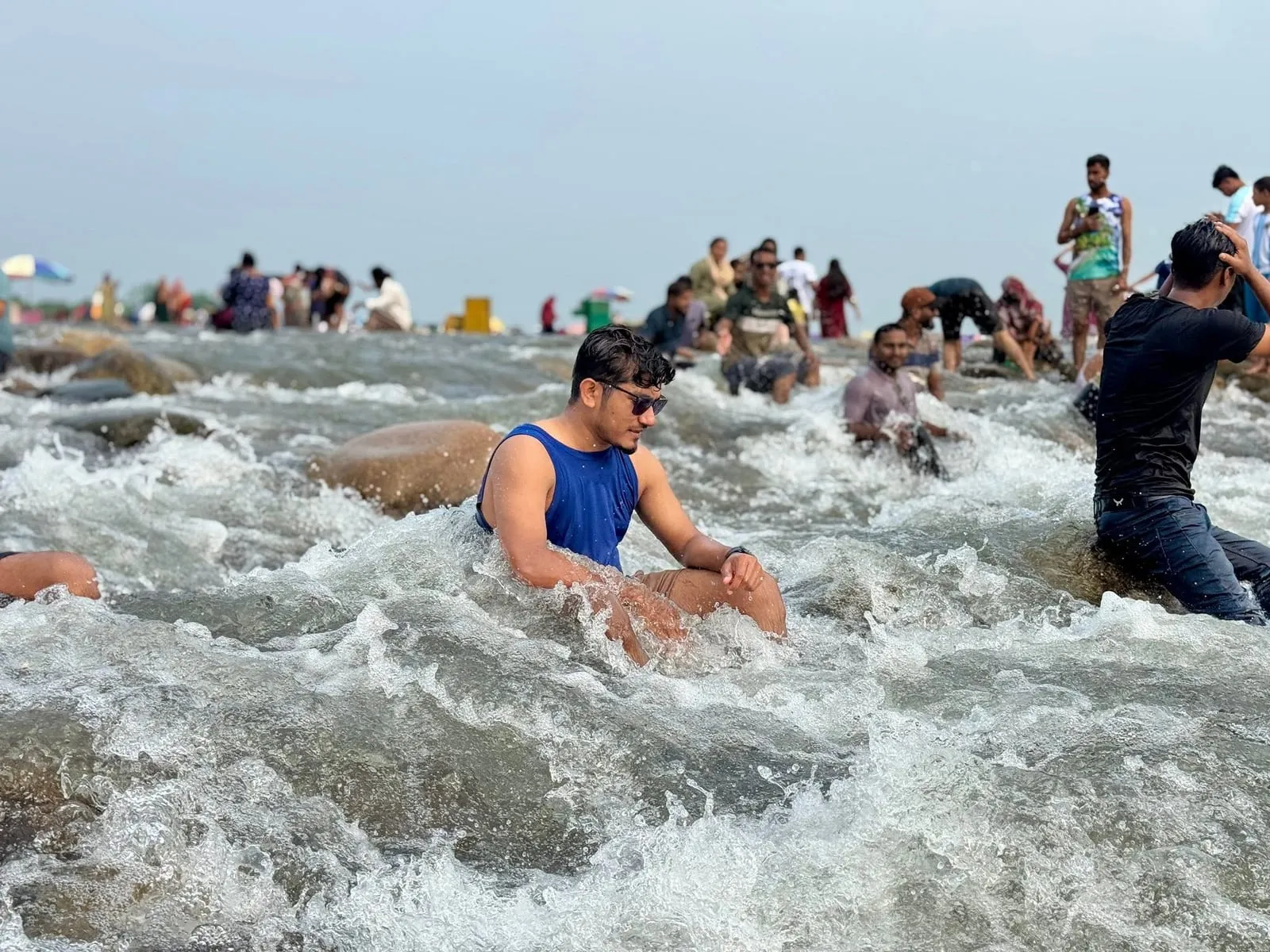 Shakawat Hridoy sitting in the rushing river rapids at Bichanakandi, Sylhet, with other visitors behind him