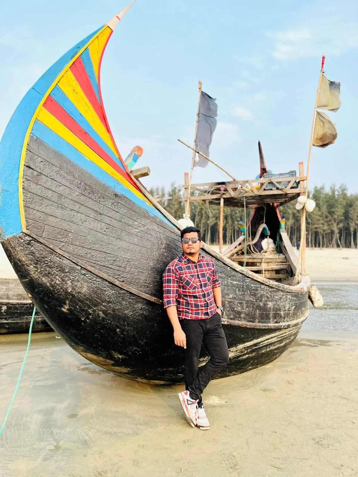 Shakawat Hridoy leaning on a painted wooden fishing boat on the beach at Cox's Bazar