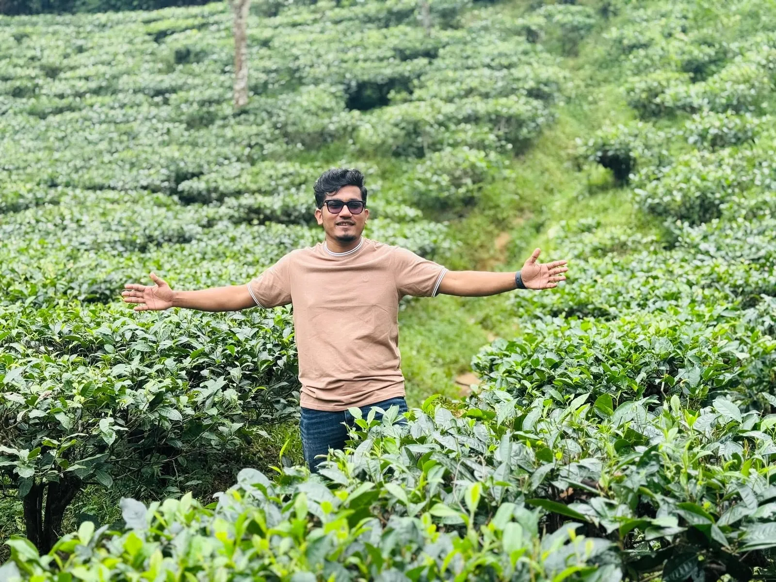 Shakawat Hridoy with his arms wide among the rows of a tea garden in Sylhet